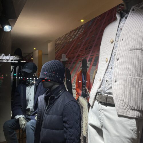 Schaufenster mit eleganten, dunklen Schaufensterpuppen in Winterkleidung vor einem städtischen Hintergrund.