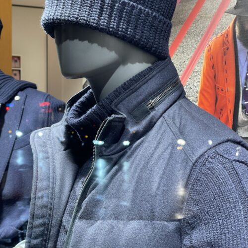 Eine graue Schaufensterpuppe mit neutralem Ausdruck trägt eine dunkelblaue Strickjacke und Mütze.