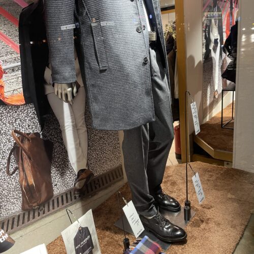 Mann in grauem Anzug und schwarzen Schuhen, steht in einem stilvollen Schaufenster.